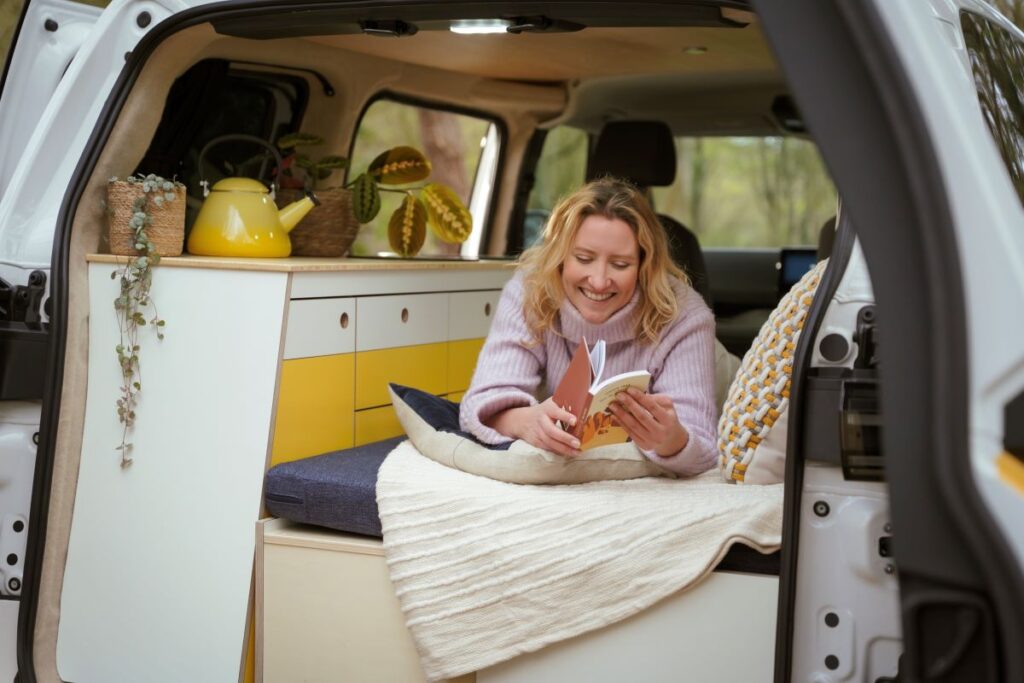 A person reading a book in their VW ID Buzz campervan at a campsite